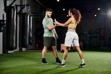Erkek bir antrenör, spor salonunda bir kadına kendini savunma teknikleri gösterir. Gücünü ve gücünü gösterir..