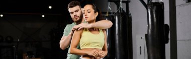 Erkek bir antrenör, spor salonunda bir kadına savunma teknikleri öğretiyor. Dayanışma ve güç gösterisi yapıyor..