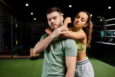 Erkek bir antrenör, bir kadına spor salonunda kendini savunma tekniklerini öğreterek destek ve güç gösterisi yapar..