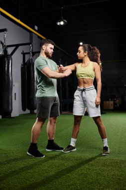 Bir erkek antrenör, spor salonunda bir kadına savunma teknikleri öğretir..