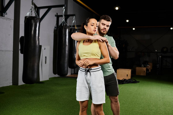 A male trainer teaches self-defense techniques to a woman in a gym, focusing on strength and empowerment.