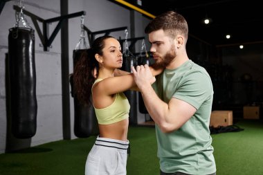 Bir erkek eğitmen, spor salonunda bir kadına kendini savunma tekniklerini öğretiyor..