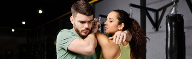 Erkek bir antrenör, spor salonunda bir kadına savunma teknikleri öğretiyor..
