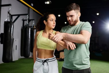 Bir erkek antrenör, spor salonunda hareket eden ve kendine güvenen bir kadına savunma teknikleri öğretir..