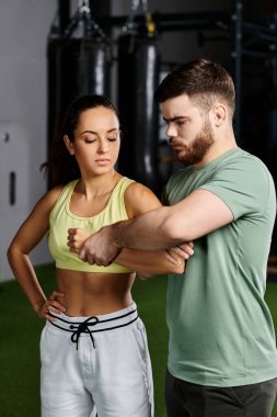 A male trainer demonstrates self-defense techniques to a woman in a gym setting. clipart