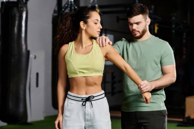 Erkek bir antrenör spor salonunda bir kadına kendini savunma teknikleri gösterir. Formda kalmak için birlik ve güç gösterir..