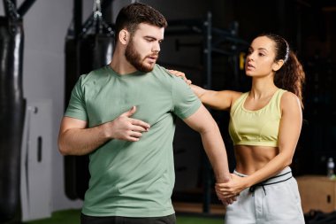 Erkek bir antrenör, bir spor salonunda kadına kendini savunma tekniklerini öğretiyor, odaklanmış ve kararlı..