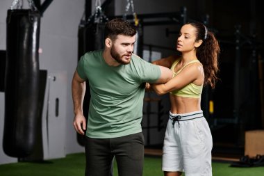 Bir erkek antrenör modern spor salonunda spor aletleriyle dolu bir kadına ustaca savunma teknikleri öğretiyor..