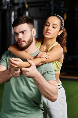 Bir erkek spor salonunda kadına kendini savunma tekniklerini gösteriyor..
