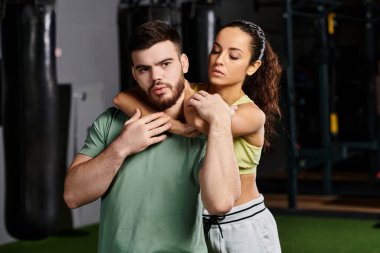 Erkek bir antrenör, spor salonundaki bir kadına kendini savunma teknikleri gösterir. Destek ve güç gösterisi yapar..
