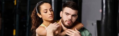 Erkek bir antrenör, spor salonunda kendini savunma teknikleri gösteren bir kadını kollarına alır..