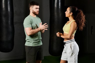 Bir erkek antrenör, spor salonunda bir kadına kendini savunma teknikleri gösterir..