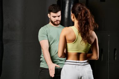 Bir erkek antrenör, spor salonunda bir kadına kendini savunma teknikleri gösterir..
