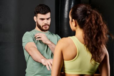 Erkek bir antrenör, spor salonunda bir kadına kendini savunma teknikleri gösterir..