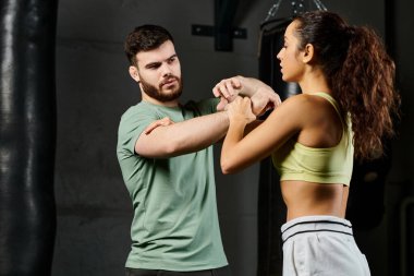 Erkek bir antrenör, spor salonunda bir kadına kendini savunma teknikleri gösterir..