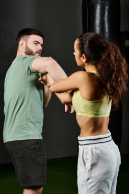 Bir erkek antrenör, spor salonunda bir kadına savunma teknikleri öğretir..