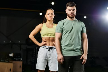 Erkek bir antrenör, spor salonunda yan yana duran bir kadına savunma teknikleri öğretiyor..