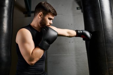 Siyah kolsuz tişörtlü yakışıklı ve boks eldivenli adam spor salonunda bir torbayı vahşice yumrukluyor..