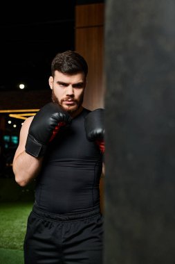 Boks eldiveni takan sakallı yakışıklı bir adam spor salonunda kum torbasının yanında antrenmana hazırlanıyor..