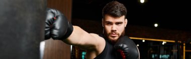 Sakallı, boks eldiveni giyen yakışıklı bir adam spor salonunda kum torbasına sert bir yumruk atıyor..