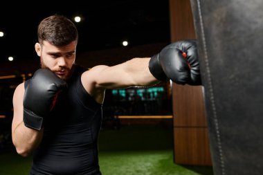 Sakallı, siyah gömlekli ve boks eldivenli yakışıklı bir adam spor salonunda torba yumrukluyor..