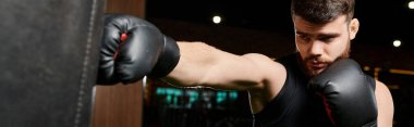 Boks eldiveni giyen sakallı bir adam spor salonundaki kum torbasına güçlü bir yumruk atıyor..