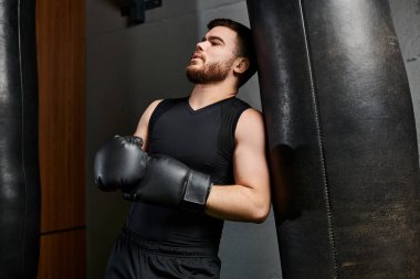 Sakallı, boks eldiveni takan yakışıklı bir adam spor salonunda torba yumrukluyor..