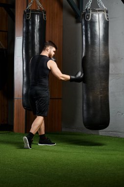 A handsome man with a beard fiercely punches a bag in a gym. clipart