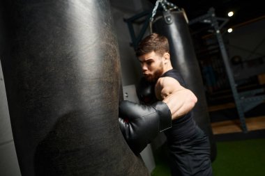 Siyah tişörtlü, boks eldivenli, sakallı yakışıklı bir adam spor salonunda torba yumruklamaya odaklanıyor..
