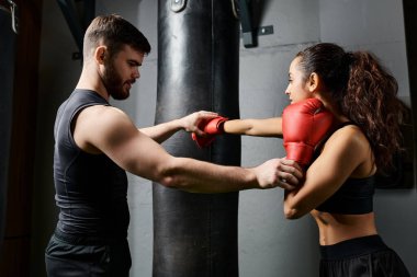 Erkek bir antrenör, spor salonunda boks yaparken aktif giyinen esmer bir sporcuya rehberlik ediyor..