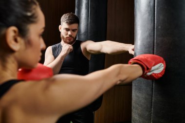 Erkek bir antrenör, spor salonunda güçlü bir boks antrenmanı yaparken aktif giyinen esmer bir sporcuyu çalıştırıyor..