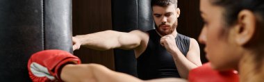 Erkek bir antrenör, spor salonundaki boks ringinde dövüşürken etkin giyimli esmer bir sporcuyu destekler..
