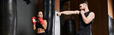 A male trainer supports a brunette sportswoman as they spar in a boxing ring in a gym. clipart