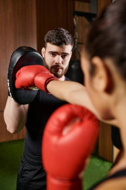 Siyah gömlekli ve kırmızı eldivenli bir kadın spor salonunda boks yapıyor..