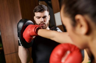 Siyah gömlekli bir kadın spor salonunda antrenman yaparken kırmızı boks eldiveni giyer..