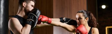 Erkek bir antrenör, spor salonunda boks yaparken aktif giyinen esmer bir sporcuya rehberlik eder..