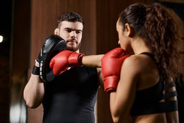 Erkek bir antrenör, esmer bir sporcuyu spor salonunda boks maçında çalıştırır..