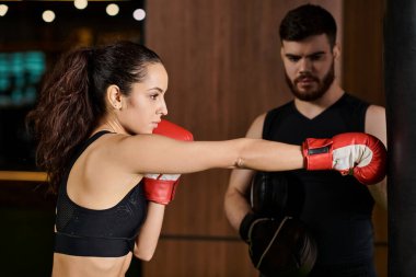 A male trainer cheers on a brunette sportswoman as they spar in a boxing ring at the gym. clipart