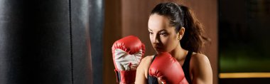 Siyah askılı ve kırmızı boks eldivenli esmer bir sporcu spor salonunda antrenman yaparken gücünü ve kararlılığını gösteriyor..