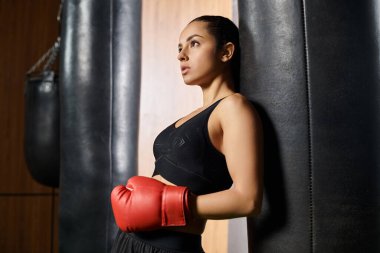 Esmer bir sporcu kadın spor salonunda siyah bluz ve parlak kırmızı boks eldivenleri giyerek güç ve güç gösterisi yapıyor..