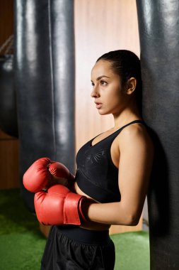 Siyah bluzlu ve kırmızı eldivenli esmer bir sporcu spor salonunda antrenman ve boks yapıyor..