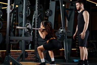 A personal trainer guides a brunette sportswoman as they both perform squats in a gym. clipart