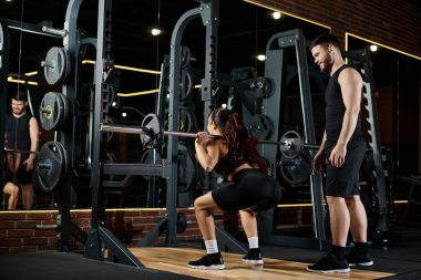 A personal trainer and a brunette sportswoman synchronously perform squats in a well-equipped gym. clipart
