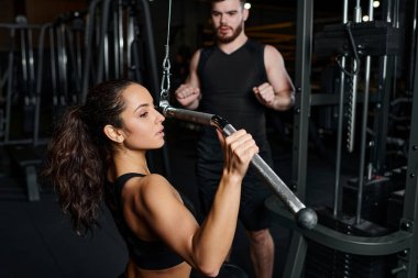 Erkek bir antrenör ve esmer bir sporcu spor salonunda birlikte çalışırken görülüyor, odaklanmış ve kararlı..