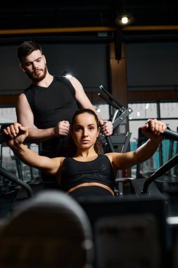 Erkek bir antrenör, esmer bir sporcuya spor salonunda spor yaparken yardımcı oluyor..