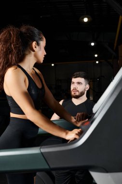 Erkek bir antrenör spor salonunda esmer bir sporcuya koşu bandında yardım ediyor..