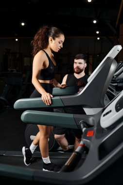 A male personal trainer and a brunette sportswoman are energetically running on a treadmill in a gym. clipart