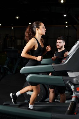 Erkek bir antrenör esmer bir sporcuyu spor salonunda koşu bandında koşarken motive eder..
