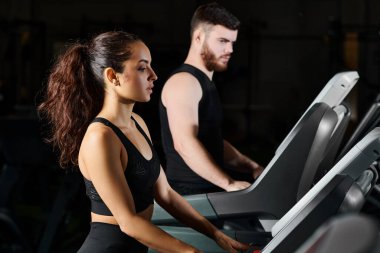 Erkek bir antrenör ve esmer bir sporcu spor salonunda koşu bandında koşarken kendilerini tüketiyorlar..