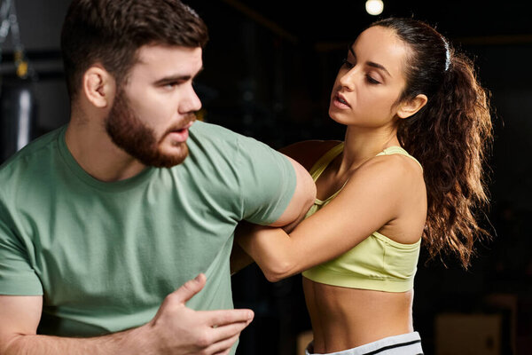 A male trainer demonstrates self-defense techniques to a woman in a gym setting.